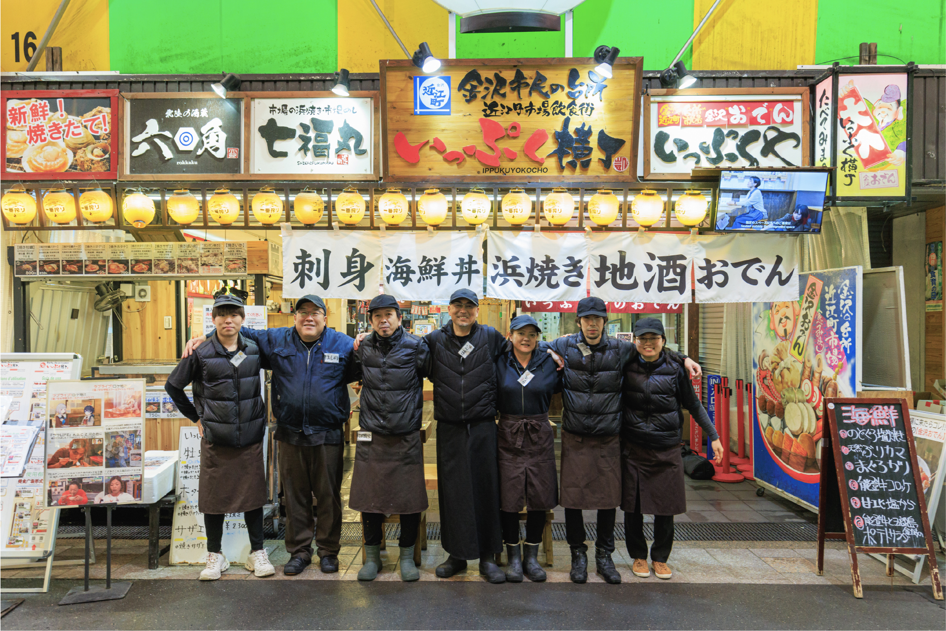 市場の飲食店『いっぷく横丁』の前で肩を組むスタッフたちの集合写真
